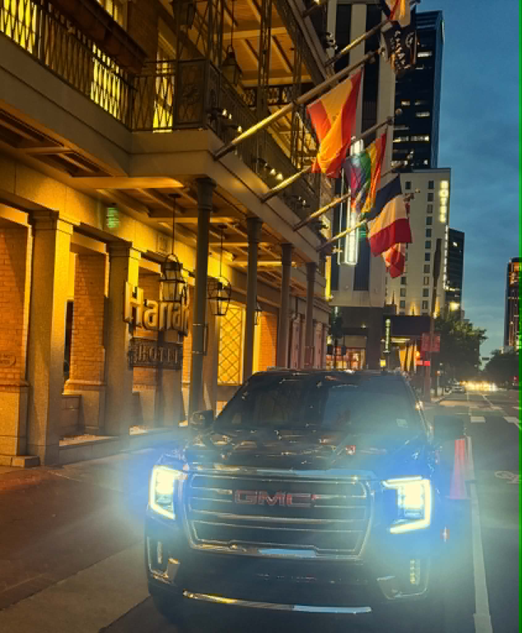 Black GMC Yukon with headlights on in front of a New Orleans hotel at night
